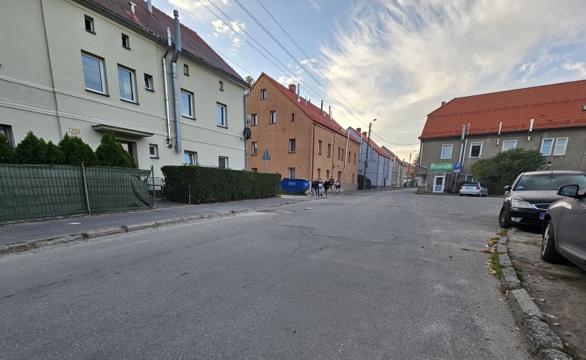 Droga asfaltowa, po bokach domy, chodnikiem idzie grupka dzieci