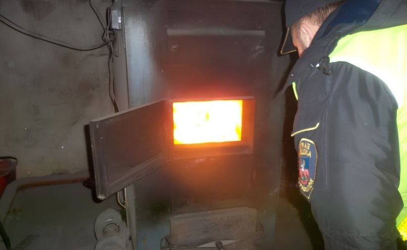 Strażnik miejski w żółtej kamizelce zaglądający do wnętrza pieca
