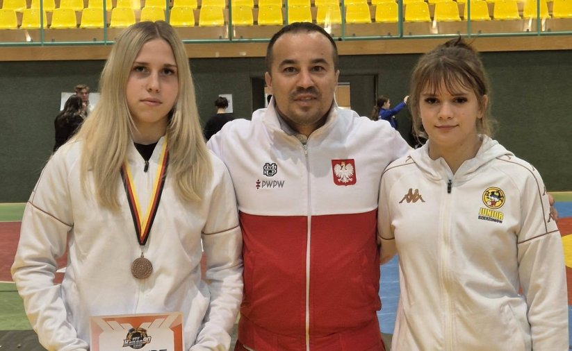 Trener w biało-czerwonej bluzie, po bokach dwie zawodniczki 