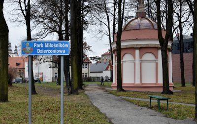 Park, po lewej tabica z nazwą Park Miłośników Dzirżowniowa, w drugim planie okrągła kaplica