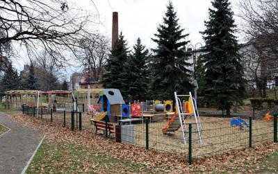 Widok na ogrodzony plac zabaw, na drugim planie drzewa