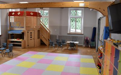 Sala zabaw z kolorową matą na podłodze i drewnianym domkiem w drugim planie