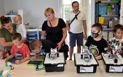 Grupa dorosłych i dzieci prszy stołach z miniaturowymi robotami