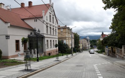 Kamienica z patelową elewacją, droga, po drógiej stronie zieleń drzew