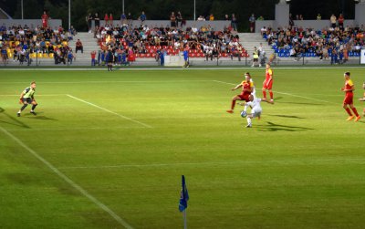 Piłkarze grający mecz na stadionie, w drugim planie trybuny z kibicami