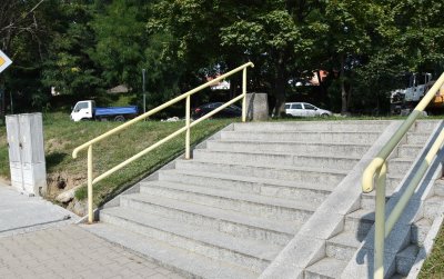 Kamienne schody, po bokach żółte poręcze w tle park