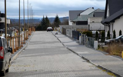 Osiedlowa ulica z kostki betonowej, wdłuż ulicy domy jednorodzinne