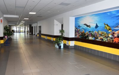 Szeroku korytarz szkolny, na ścianie po prawej bardzo duże zdjęcie rafy koralowej z rybami