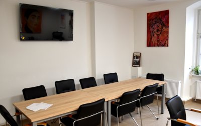 Stół i czarne krzesła, na białych ścianach obraz i telewizor