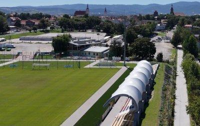 Boisko do piłki nożnej, zadaszone trybuny, za nimi chodnik