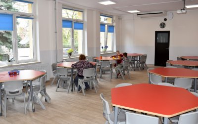 Sześciokątne stoły przy jednym troje uczniów jedzących obiad