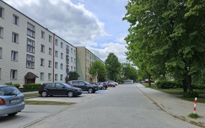 Droga z kostki brukowej po lewej czteropiętrowy blok, po prawej drzewa