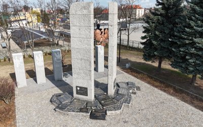 Plac z kostki, pomnik w postaci dwóch kolumn, między nimi duże godło