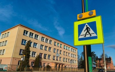 Znak drogowy z mężczyzną przechodzącym przez pasy, w tle budynek