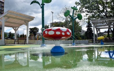 Wodny plac zabaw, na głównym planie czerwony grzybek w baiałe kropki, z którego leci woda