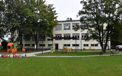 Dwupiętrowy budynek żłobka z nową piaskową elewacją, przed budynkiem plac zabaw