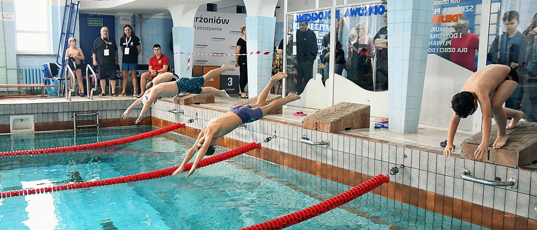 Basen kryty, młodzi zawodnicy skaczący ze stopni do wody