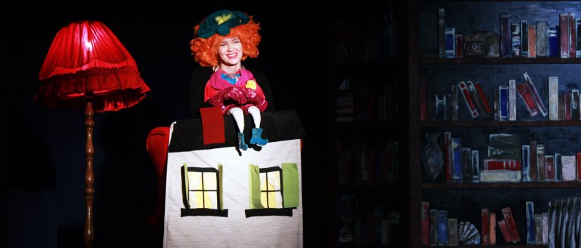Scena, duża czerwona lampa obok makieta domu, nad nią aktorka z czerwonymi włosami