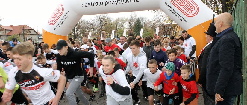 Tłum uczestników przebiega przez dmuchaną bramę startową, na niej napis Dizerżoniów nastraja pozytywnie