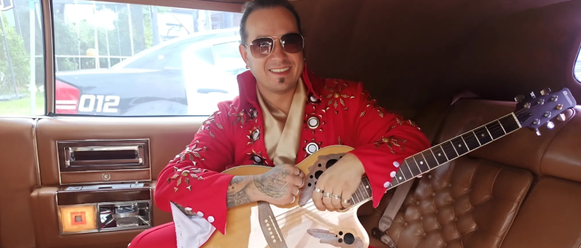 Artysta w czerwonym stroju Elvisa i z gitarą siedzący we wnętrzu auta