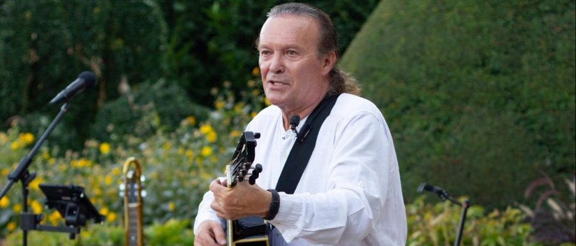 Janusz Credo w białej koszuli z gitarą akustyczną