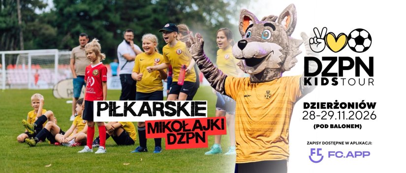 Dzieci siedzące i stojące na boisku obok maskotka w postaci wilka z uniesionymi do góry rękoma